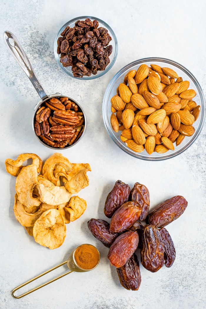 Raisins, almonds, pecans, dried apples, dates and cinnamon on a table.