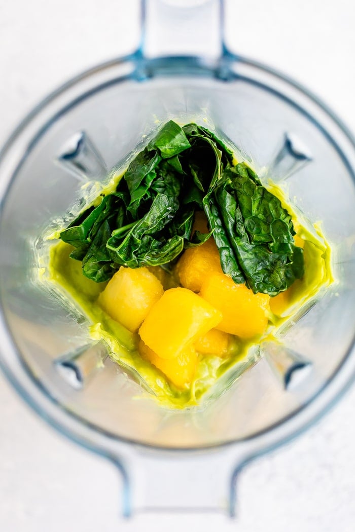 Overhead photo of a blender with kale, pineapple and mango.