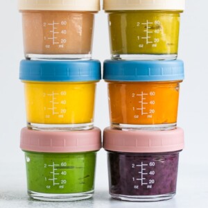 Stack of 6 glass baby food jars filled with homemade different baby foods.