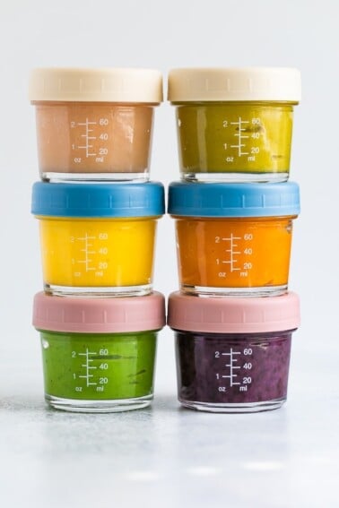 Stack of 6 glass baby food jars filled with homemade different baby foods.
