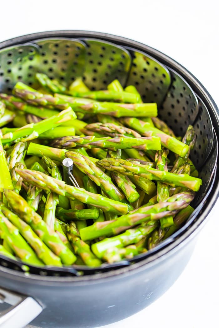 Asparagus spears in a steamer basket in a pot.