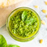 Overhead photo of a glass jar full of homemade pesto with fresh basil leaves on the top.