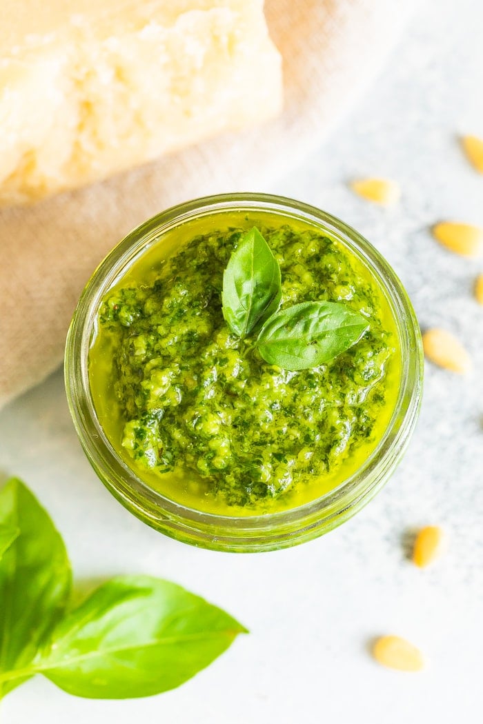 Overhead photo of a glass jar full of homemade pesto with fresh basil leaves on the top.