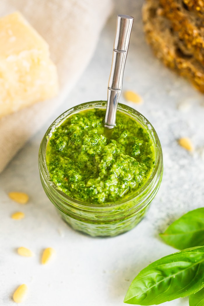 Overhead photo of a glass jar full of homemade pesto with a silver spoon in the jar.