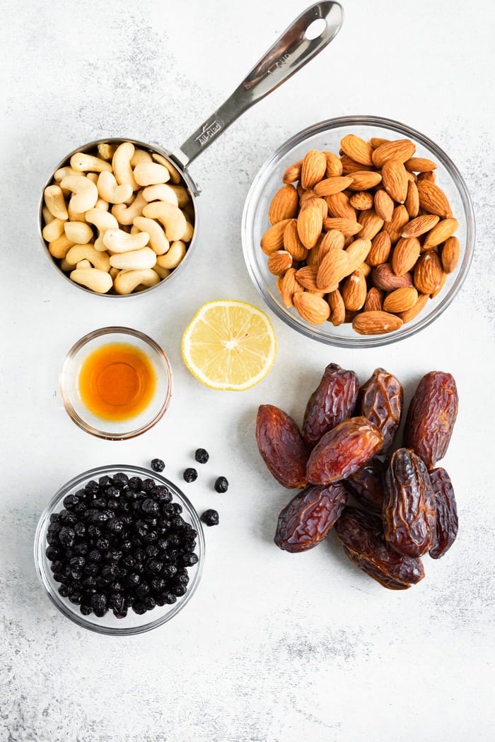 Cashews, almonds, lemon, vanilla, dates and dried blueberries on a table.
