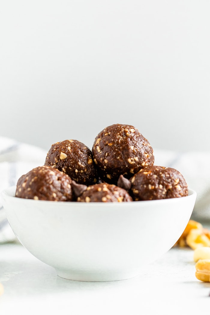 White bowl full of brownie energy balls. Cashews are on the table beside the bowl.