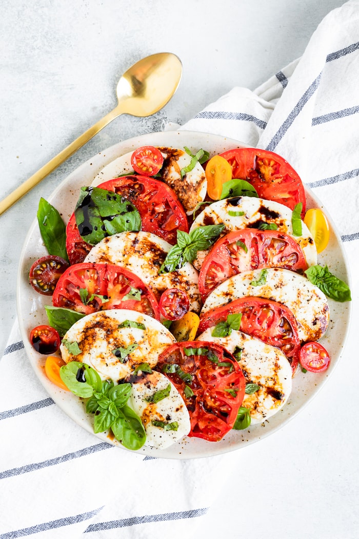 Caprese salad on a plate. A dish cloth and gold spoon are beside the plate.