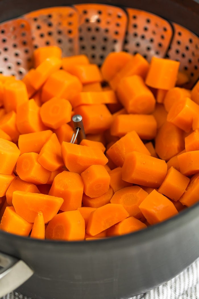 Cooked chopped carrots in a steamer basket in a Calphalon pot.