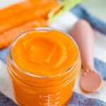 Glass baby food jar with carrot puree and an ezpz spoon off to the side.