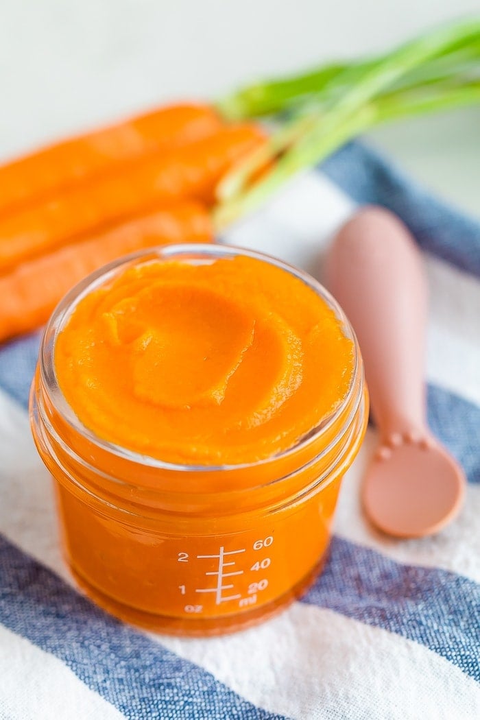 Glass baby food jar with carrot puree and an ezpz spoon off to the side.