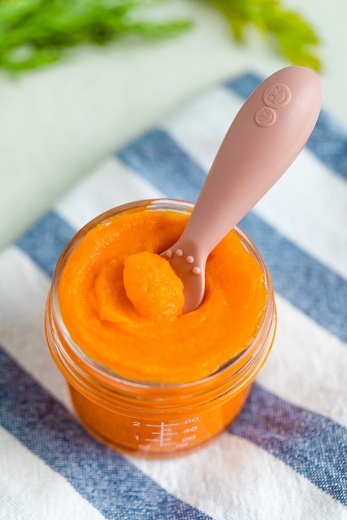 Glass baby food jar with carrot puree with an ezpz spoon dipped in.