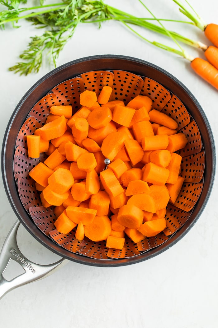 Raw chopped carrots in a steamer basket in a Calphalon pot.