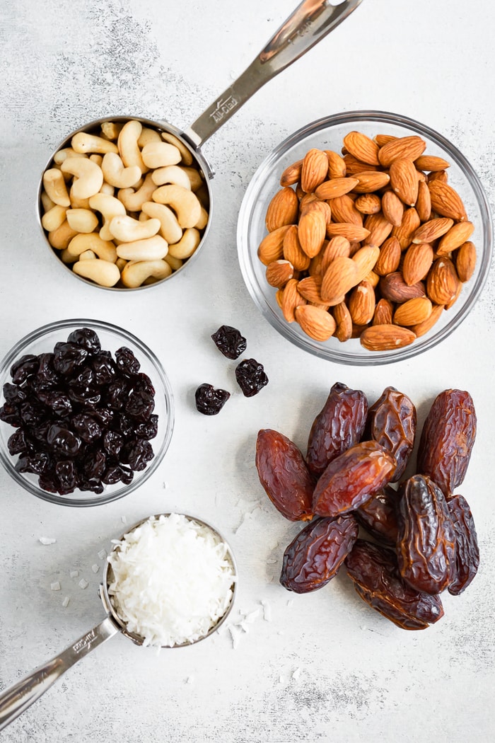 Cashews, almonds, dried cherries, coconut and dates measured out on a table.