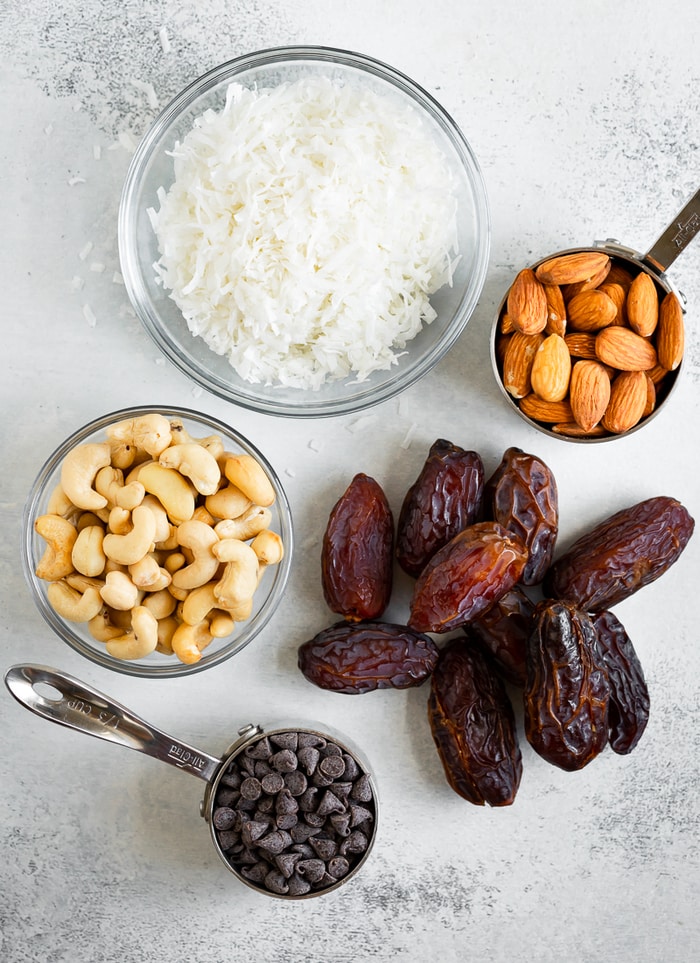 Coconut flakes, almonds, cashews, dates and chocolate chips on a table.