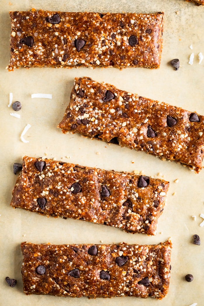 4 homemade chocolate chip Larabars on parchment paper surrounded by chocolate chips and coconut flakes.