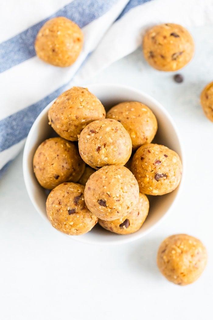 Bird's eye view of a bowl full of cookie dough protein balls and protein balls on the table surrounded by a cloth.