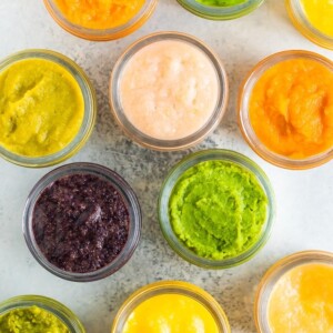 Overhead photo of glass baby food jars filled with 6 different types of homemade baby food.