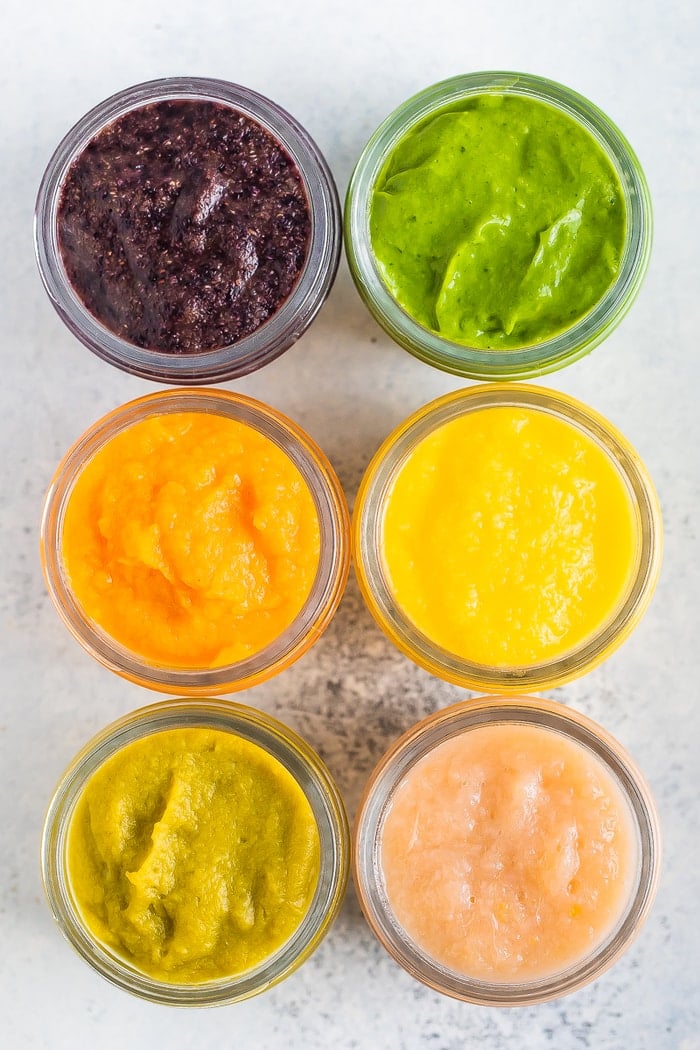Overhead photo of 6 baby food glass jars with 6 different kind of baby food with labels of what kind of food is inside.