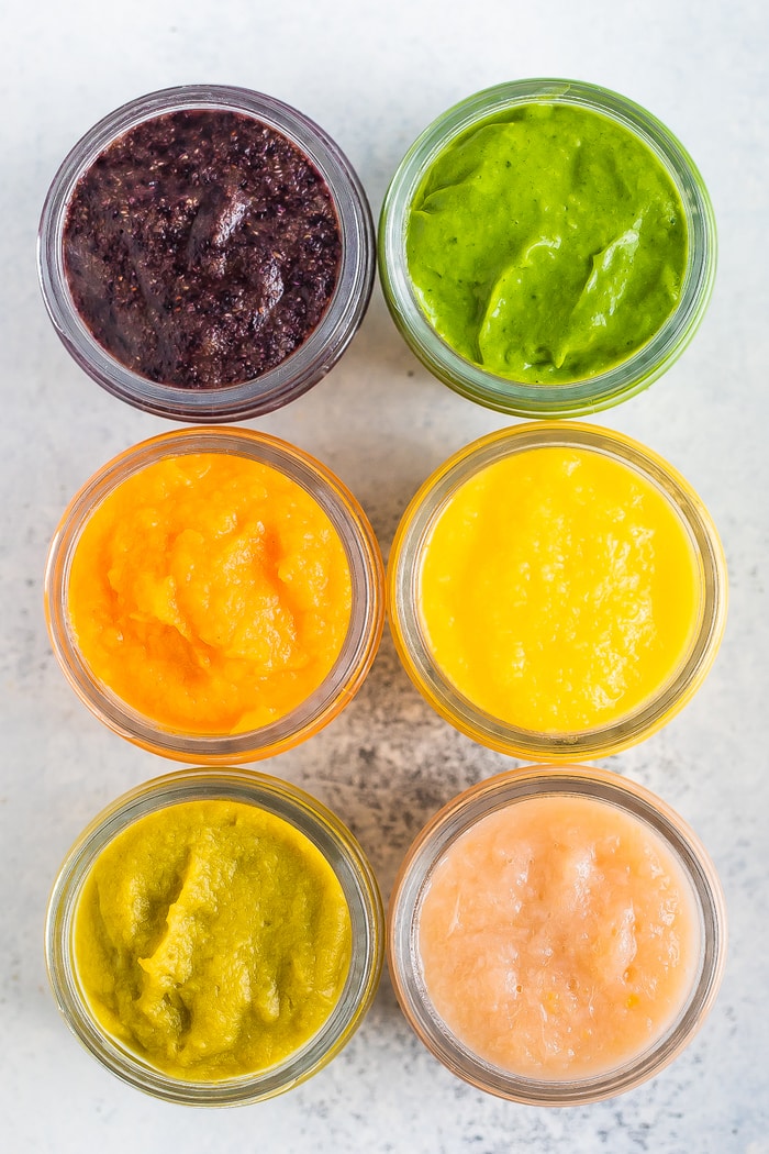 Overhead photo of 6 baby food glass jars with 6 different kind of baby food with labels of what kind of food is inside.