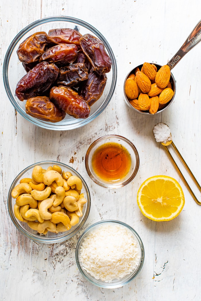 Ingredients to make lemon energy balls on a table: bowls of dates, vanilla, cashews, almonds, coconut, lemon and sea salt.