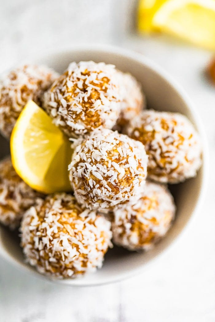 Bowl full of lemon energy balls rolled in coconut flakes. Slice of lemon is in the bowl.