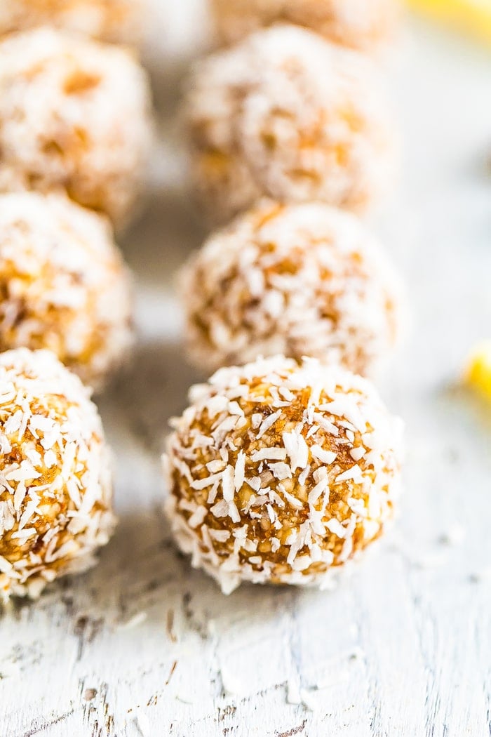 6 lemon energy balls coated in coconut on a wood white table top.