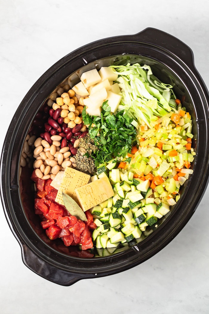 Slow cooker filled with ingredients for minestrone soup. 