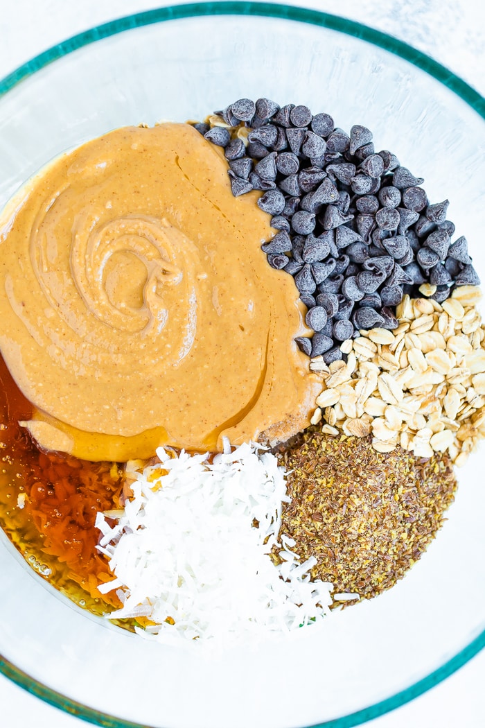 Glass mixing bowl with honey, coconut flakes, flax, oats, chocolate chips and peanut butter.