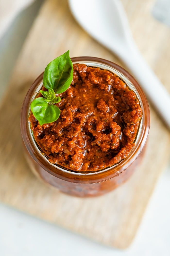 Bird's eye view of a jar of sun-dried tomato pesto topped with a sprig of fresh basil.