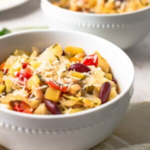A white bowl with minestrone soup with shredded parmesan on top.