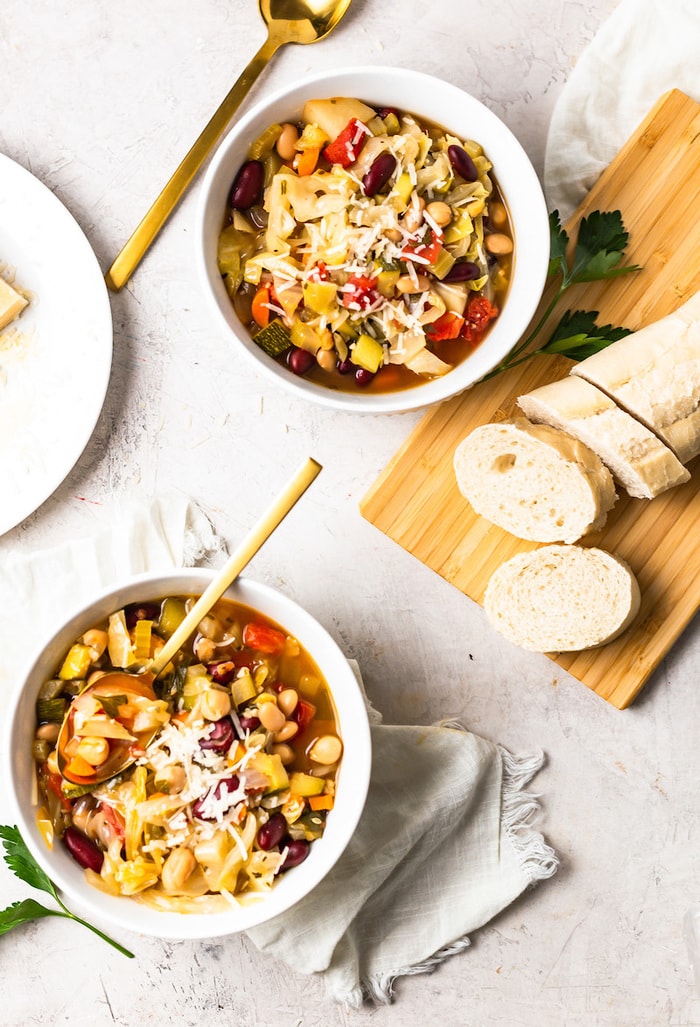 Two bowls of minestrone soup with gold spoons. 