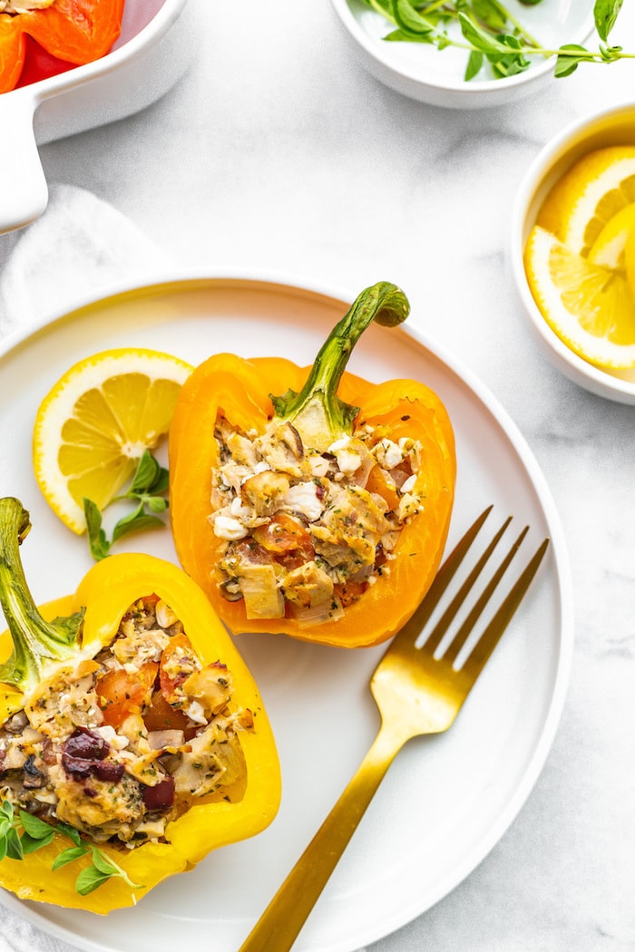 Two tuna stuffed bell peppers on a plate with a gold fork and a lemon slice.