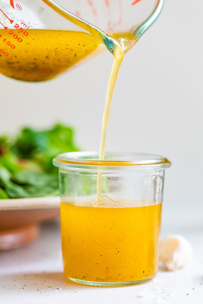 Glass measuring cup pouring white balsamic vinaigrette into a glass jar.