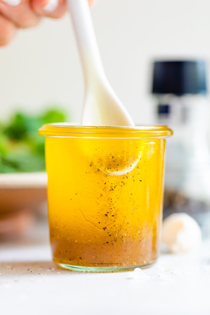 White spoon stirring a jar white balsamic vinaigrette.