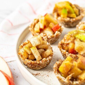 Mini raw apple pies on a plate. A napkin and apple slices are also on the table.