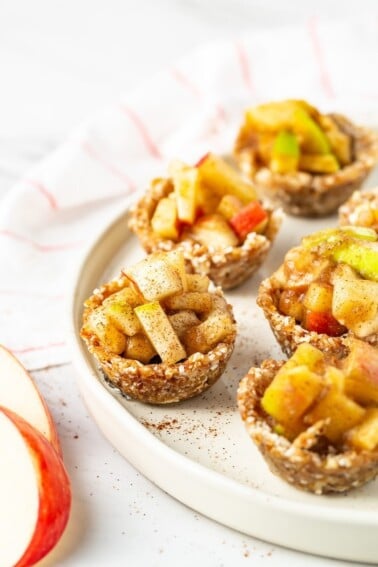 Mini raw apple pies on a plate. A napkin and apple slices are also on the table.