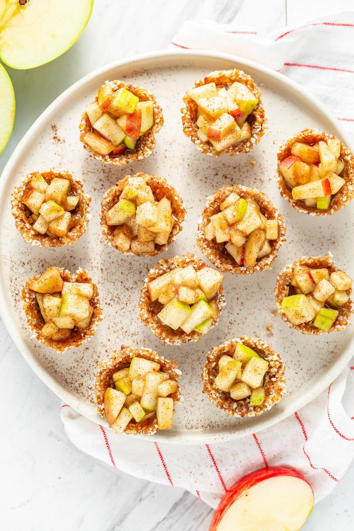 Bird's eye photo of several mini raw apple pies on a plate sprinkled with cinnamon.