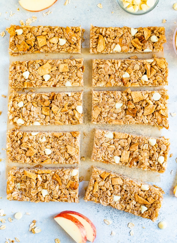10 apple granola bars on a table surrounded by bits of oats and apple slices.