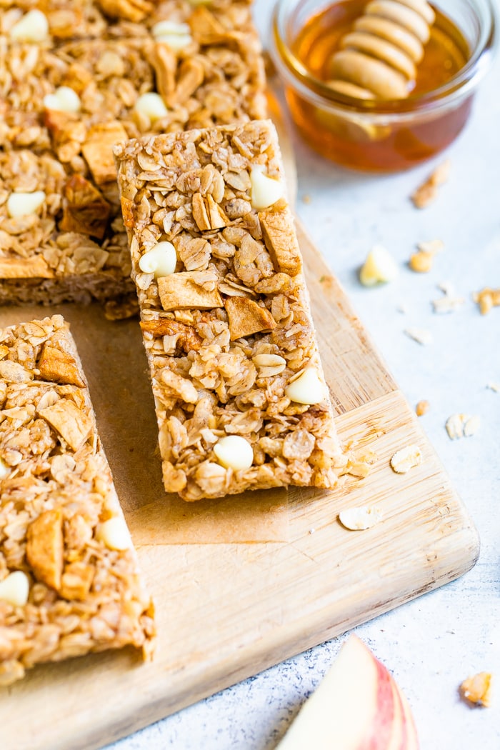 Apple granola bar on a wood cutting board next to a bowl of honey.