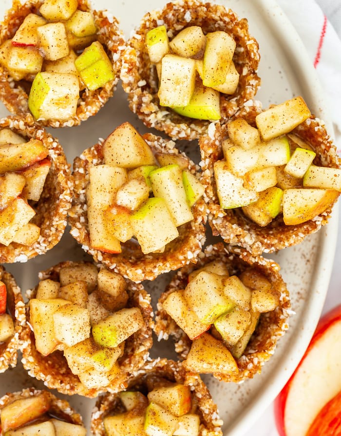 Bird's eye photo of several mini raw apple pies on a plate sprinkled with cinnamon.