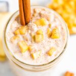 Overhead photo of a jar full of apple pie overnight oats garnished with a cinnamon stick and apple chunks.