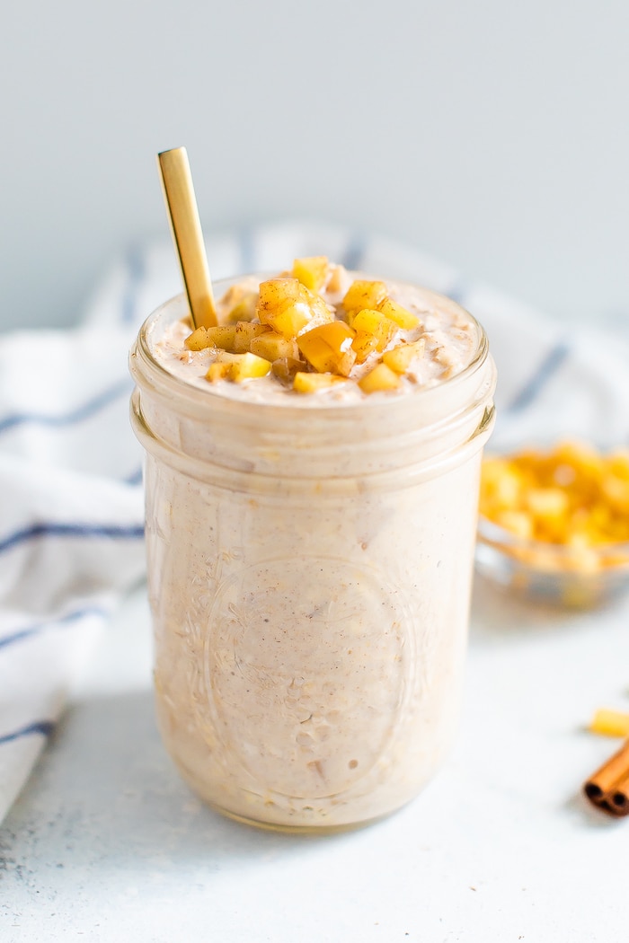 Glass jar with apple pie overnight oats topped with cinnamon apple chunks. A gold spoon is in the jar.