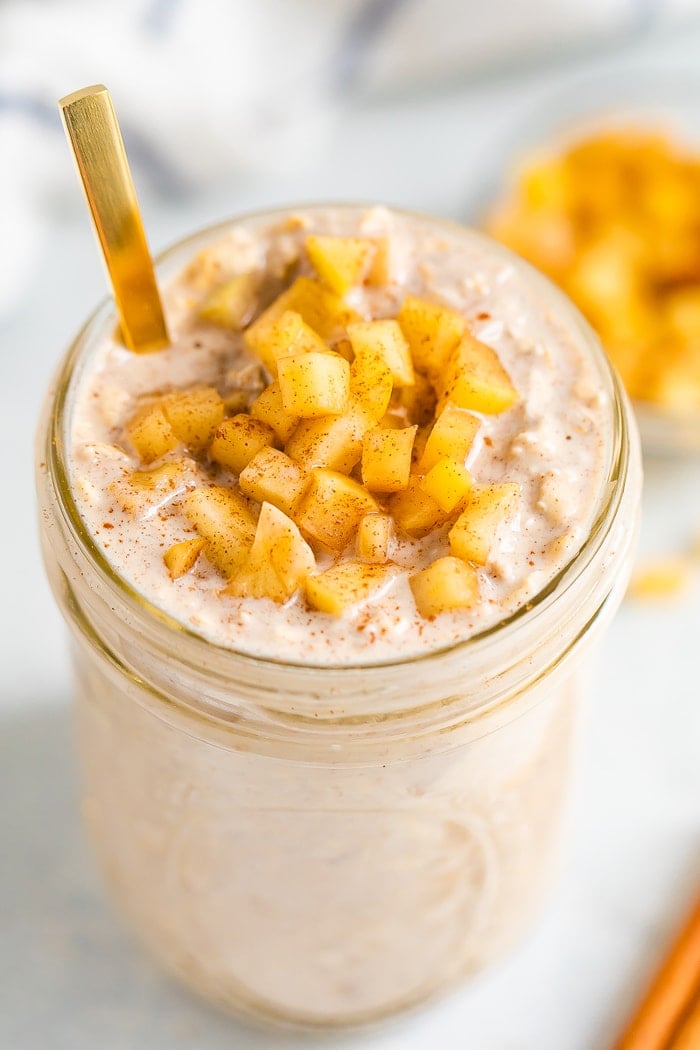 Glass jar with apple pie overnight oats topped with cinnamon apple chunks. A gold spoon is in the jar.