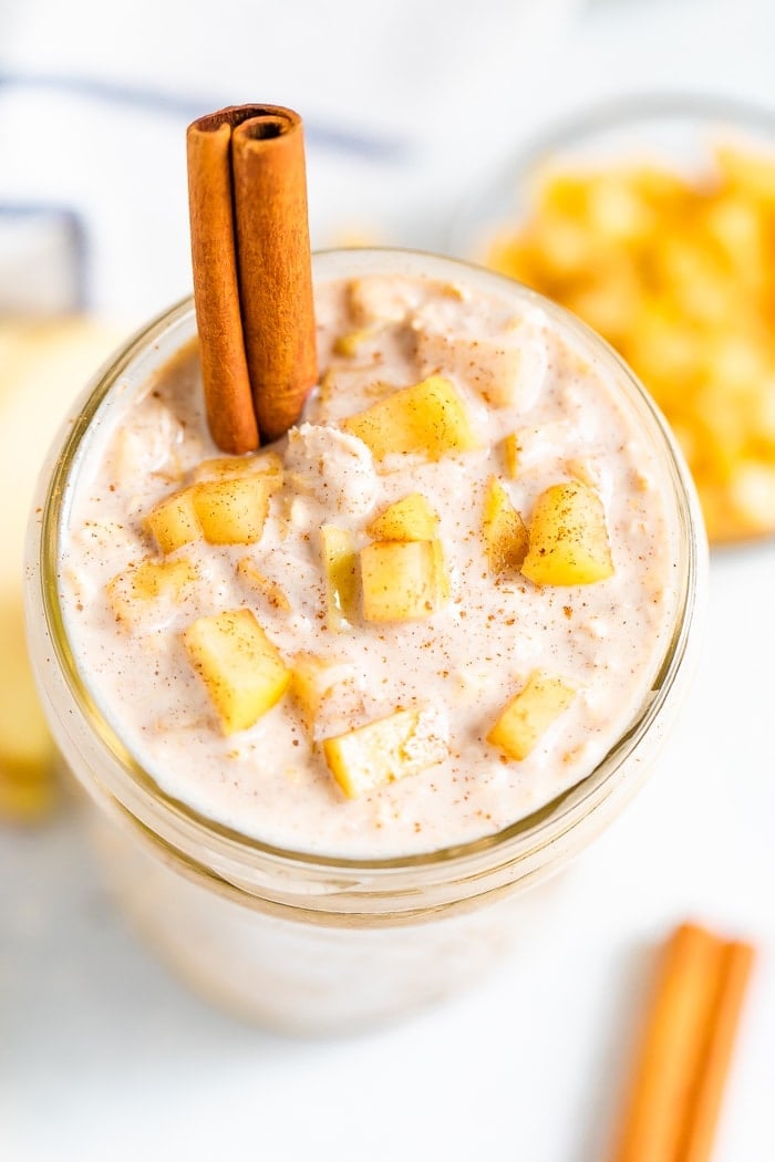 Overhead photo of a jar full of apple pie overnight oats garnished with a cinnamon stick and apple chunks.