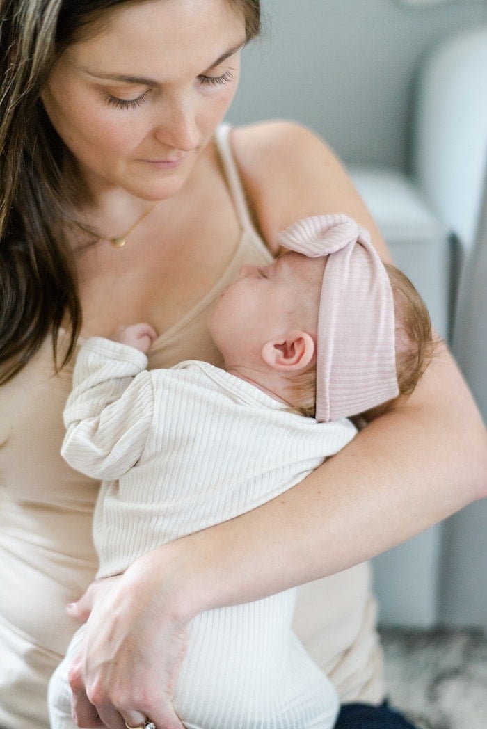 Woman holding newborn baby. Baby has a headband on. 