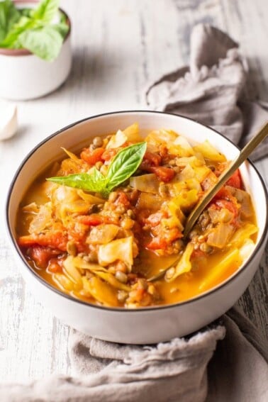 Cabbage lentil soup portioned into one bowl with gold spoon in soup.