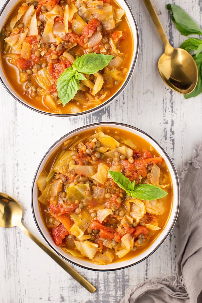 Cabbage lentil soup portioned into two white bowls with gold spoons on the side.