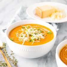 Bowl of carrot parsnip soup topped with green onion and cheese.