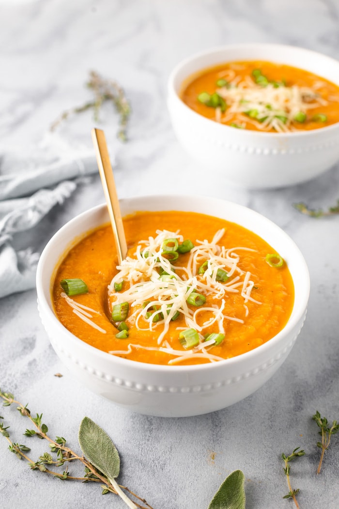 Two bowls of carrot parsnip soup topped with green onions and cheese.