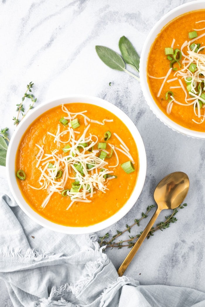 Two bowls of carrot parsnip soup topped with green onions and cheese.